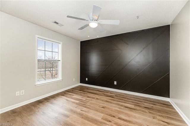 spare room featuring light wood-type flooring, visible vents, a textured ceiling, baseboards, and ceiling fan