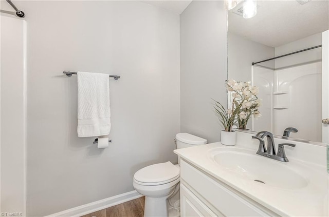 full bath with toilet, wood finished floors, baseboards, walk in shower, and vanity