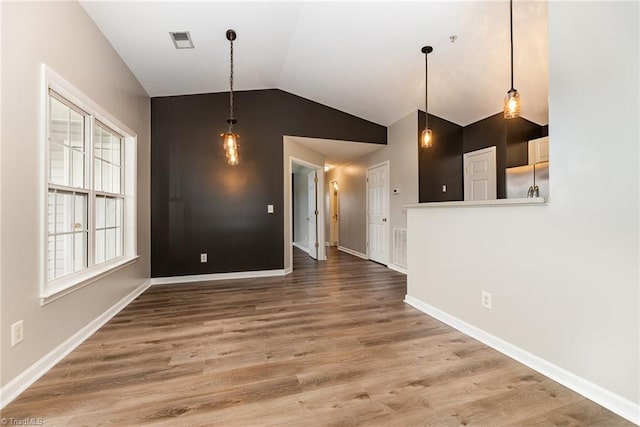 unfurnished dining area featuring visible vents, lofted ceiling, baseboards, and wood finished floors