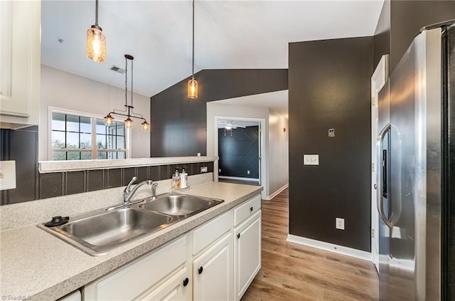 kitchen with light wood-type flooring, light countertops, vaulted ceiling, freestanding refrigerator, and a sink