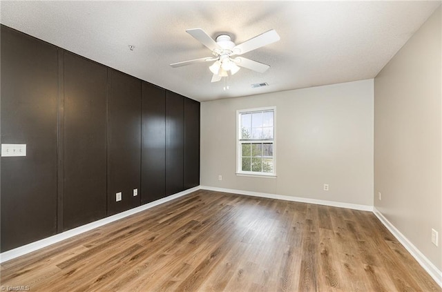 interior space featuring a ceiling fan, light wood-style floors, visible vents, and baseboards