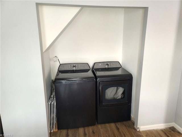 clothes washing area featuring laundry area, dark wood-type flooring, washing machine and clothes dryer, and baseboards