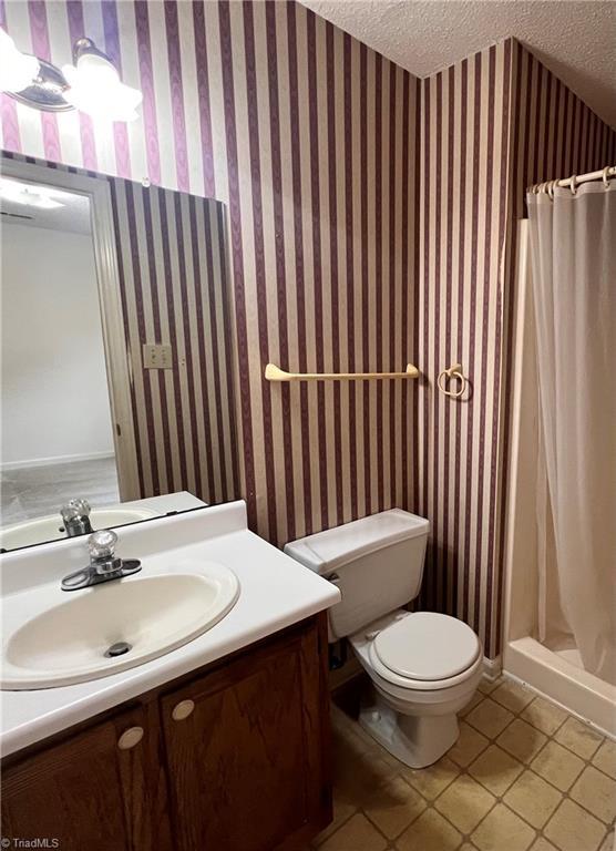 bathroom featuring a textured ceiling, a stall shower, toilet, and wallpapered walls