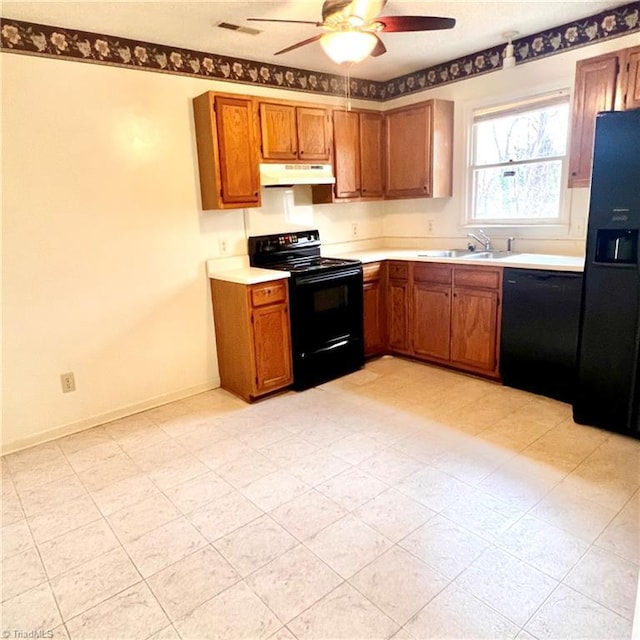 kitchen with brown cabinetry, under cabinet range hood, light countertops, black appliances, and a sink