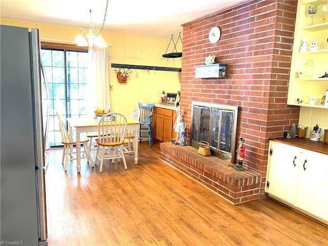 dining room featuring a notable chandelier, light hardwood / wood-style flooring, and a brick fireplace