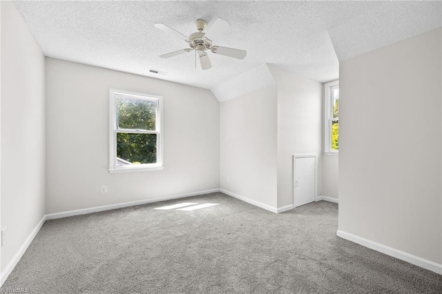 empty room with a textured ceiling, light colored carpet, vaulted ceiling, and ceiling fan