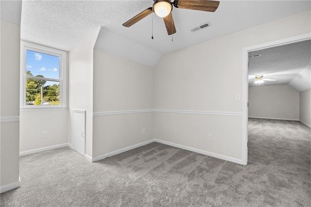 carpeted empty room with a textured ceiling, vaulted ceiling, and ceiling fan