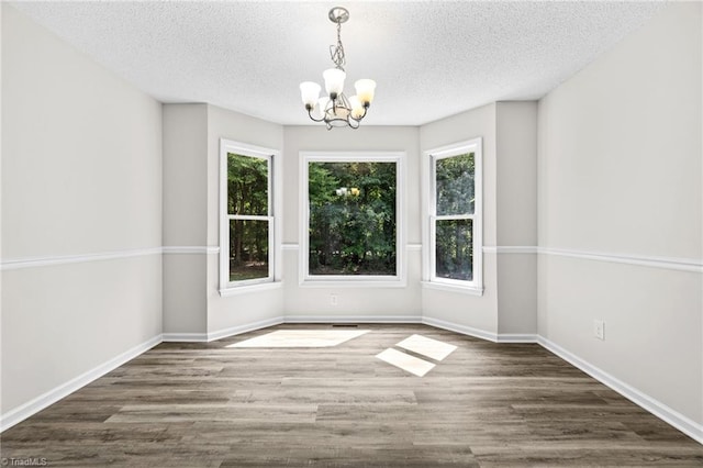 unfurnished dining area featuring a textured ceiling, dark wood-type flooring, and an inviting chandelier