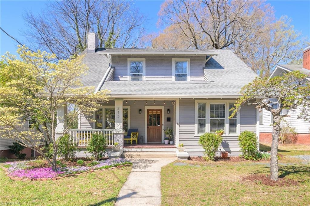 bungalow-style house with a front yard, a chimney, a shingled roof, and covered porch