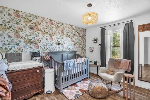 bedroom with wallpapered walls, a textured ceiling, baseboards, and wood finished floors