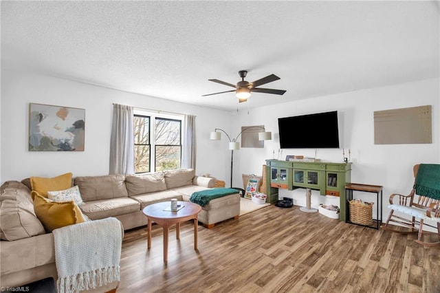 living area with a ceiling fan, a textured ceiling, and wood finished floors