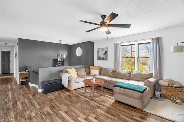 living room with a textured ceiling, ceiling fan with notable chandelier, wood finished floors, and baseboards