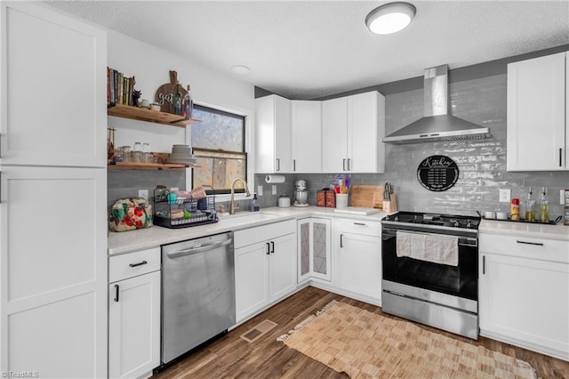 kitchen with wood finished floors, wall chimney exhaust hood, appliances with stainless steel finishes, and a sink