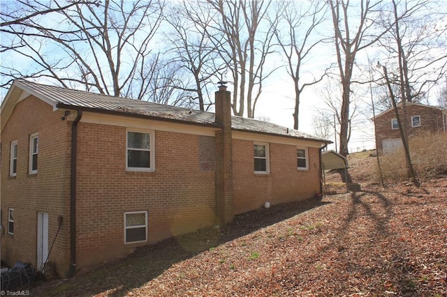 view of side of home featuring a standing seam roof, metal roof, brick siding, and a chimney