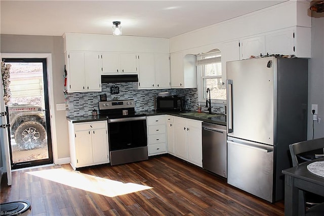 kitchen featuring dark countertops, stainless steel appliances, under cabinet range hood, white cabinetry, and a sink