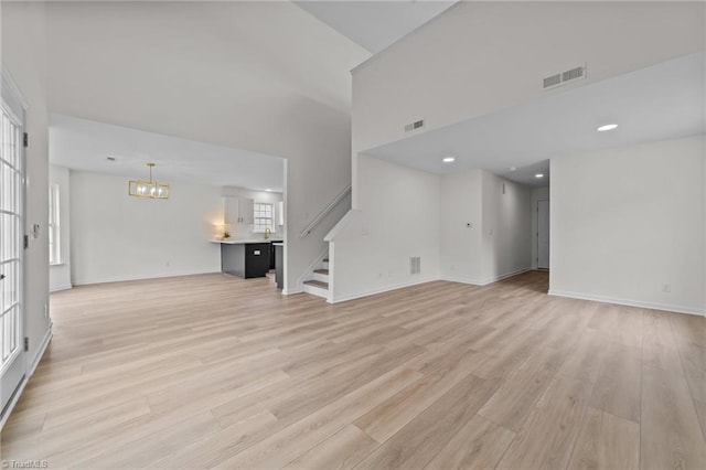 4908 Peppercorn Ln, Greensboro, NC 27406 - unfurnished living room with a chandelier, stairs, light wood-type flooring, and a towering ceiling