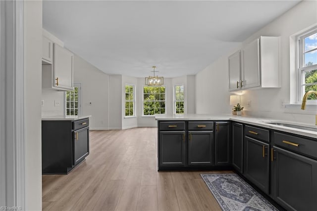 4908 Peppercorn Ln, Greensboro, NC 27406 - kitchen with a peninsula, light countertops, a chandelier, light wood-style flooring, and white cabinetry