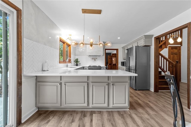 kitchen featuring a notable chandelier, light hardwood / wood-style flooring, kitchen peninsula, and stainless steel refrigerator