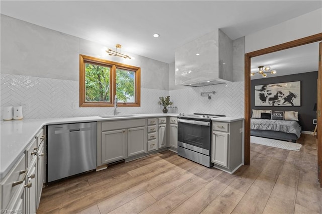 kitchen with wall chimney range hood, stainless steel appliances, sink, gray cabinets, and light hardwood / wood-style floors