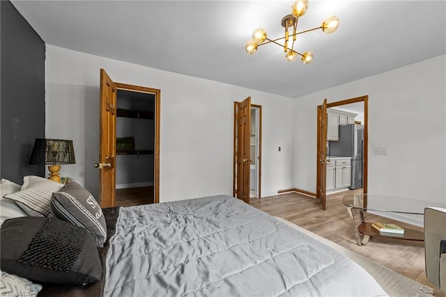 bedroom with a closet, light hardwood / wood-style flooring, a walk in closet, stainless steel fridge, and a notable chandelier