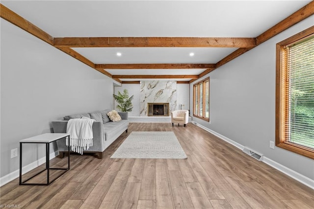 unfurnished living room featuring a high end fireplace, beam ceiling, plenty of natural light, and light wood-type flooring