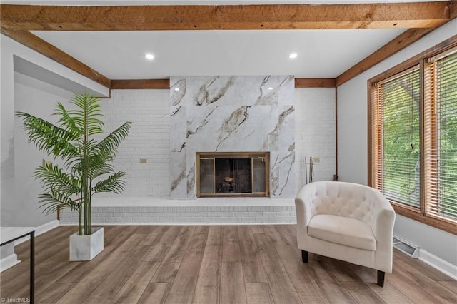 sitting room featuring a wealth of natural light, a high end fireplace, beamed ceiling, and wood-type flooring