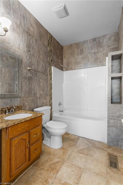 full bathroom with shower / tub combination, vanity, tile walls, and toilet