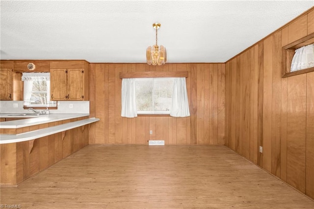 kitchen with a notable chandelier, light wood-type flooring, pendant lighting, wood walls, and kitchen peninsula