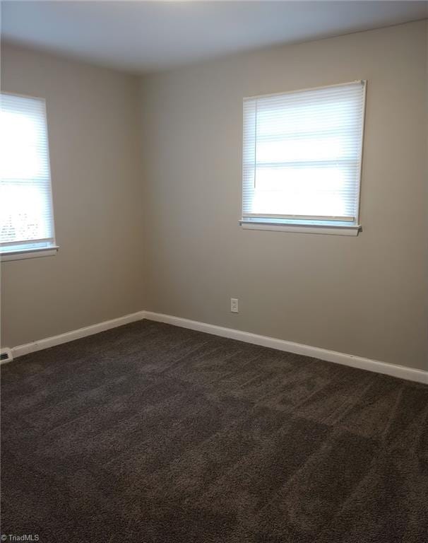 unfurnished room featuring dark carpet and a healthy amount of sunlight