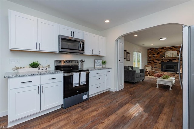 kitchen with dark wood-type flooring, open floor plan, arched walkways, appliances with stainless steel finishes, and white cabinets