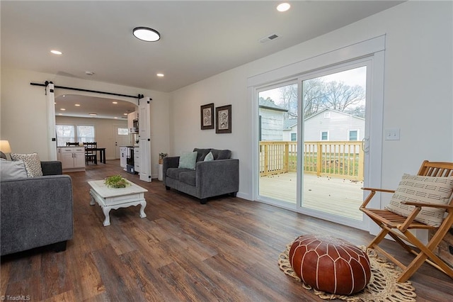 living area with a wealth of natural light, visible vents, a barn door, and wood finished floors