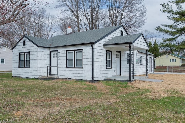 view of front of property with a shingled roof, a front yard, fence, and a chimney