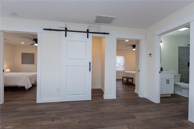 unfurnished bedroom featuring visible vents, a barn door, and dark wood finished floors