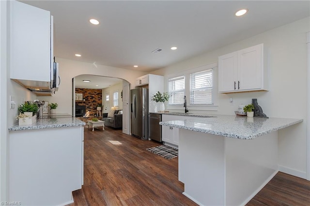 kitchen featuring dark wood-style floors, white cabinetry, stainless steel appliances, arched walkways, and a peninsula