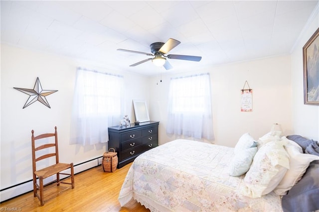 bedroom with baseboard heating, wood finished floors, a ceiling fan, and crown molding