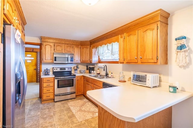 kitchen featuring a peninsula, brown cabinetry, appliances with stainless steel finishes, and light countertops