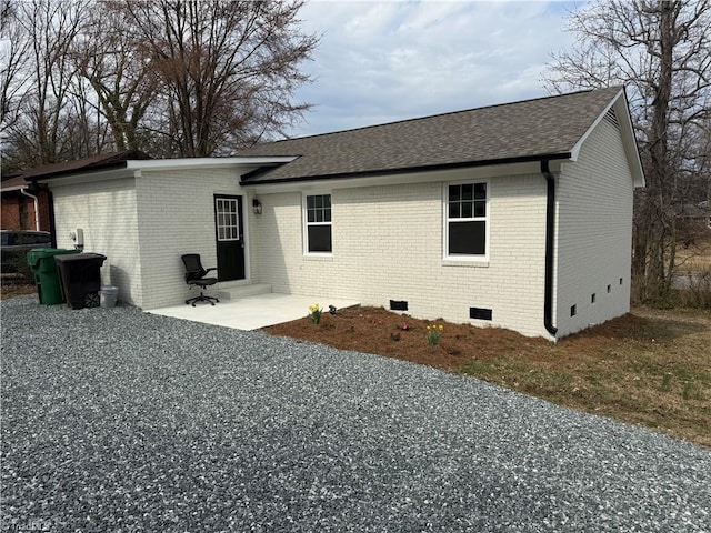 rear view of property featuring crawl space, a patio area, a shingled roof, and brick siding