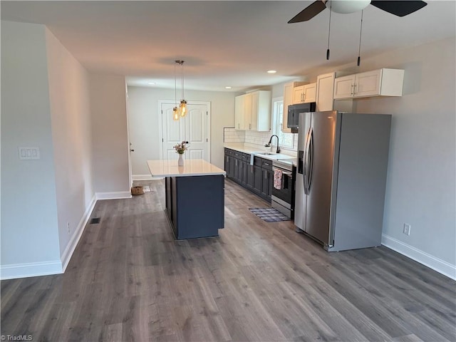 kitchen with a sink, light countertops, appliances with stainless steel finishes, a center island, and tasteful backsplash