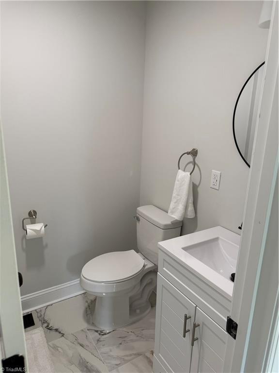 bathroom with marble finish floor, vanity, toilet, and baseboards