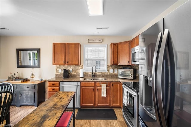 kitchen with tasteful backsplash, stainless steel appliances, light wood-style floors, a sink, and visible vents