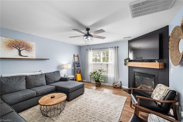 living room featuring ceiling fan, a glass covered fireplace, visible vents, baseboards, and wood finished floors
