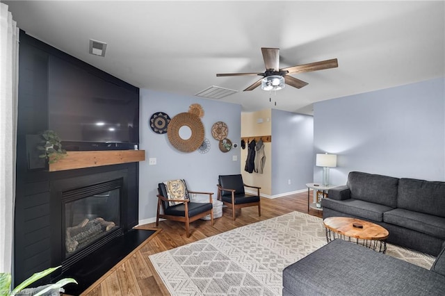 living room with wood finished floors, visible vents, and a ceiling fan