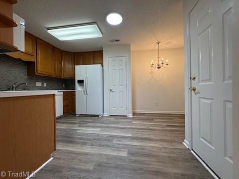 kitchen featuring backsplash, wood finished floors, light countertops, an inviting chandelier, and white appliances