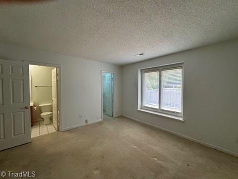 unfurnished bedroom featuring connected bathroom, a textured ceiling, baseboards, and carpet