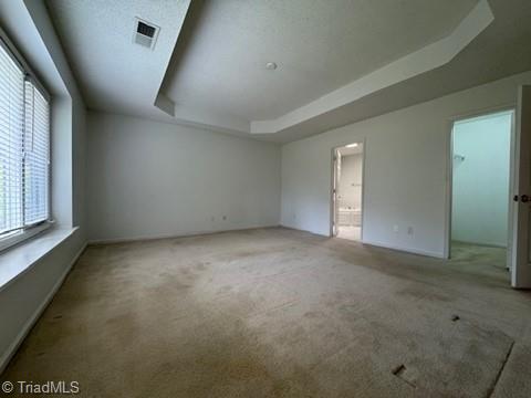 unfurnished room with visible vents, carpet flooring, baseboards, and a tray ceiling