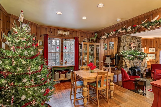 dining room with crown molding, wooden walls, wood-type flooring, and a wood stove