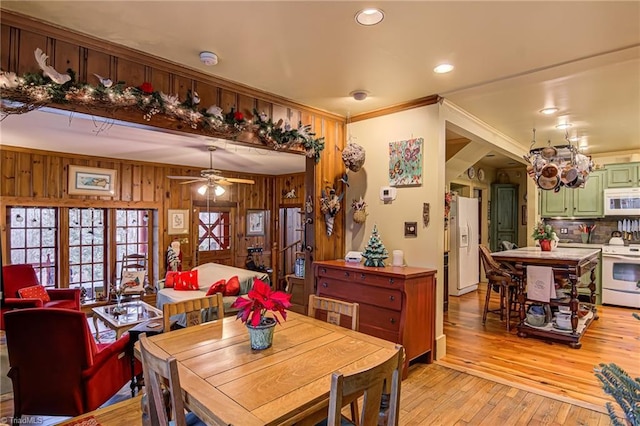 dining space with wooden walls, ornamental molding, ceiling fan, and light wood-type flooring