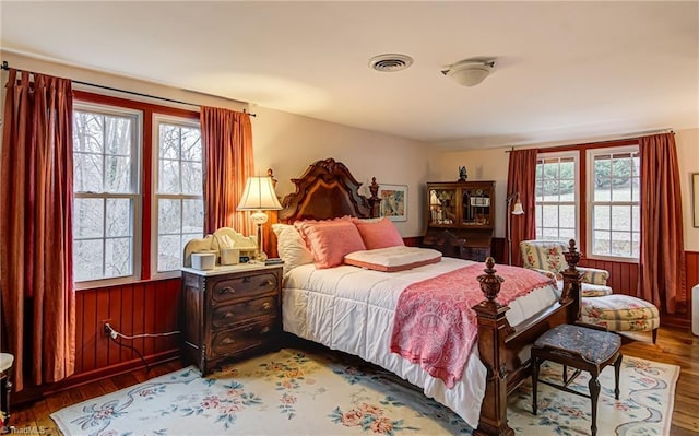 bedroom featuring multiple windows, wood-type flooring, and wood walls