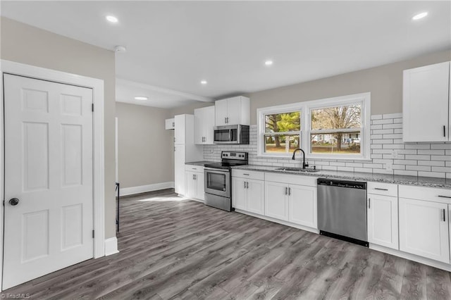 kitchen with light stone counters, a sink, appliances with stainless steel finishes, decorative backsplash, and dark wood finished floors