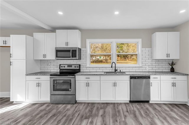 kitchen with stainless steel appliances, light stone counters, a sink, and white cabinetry